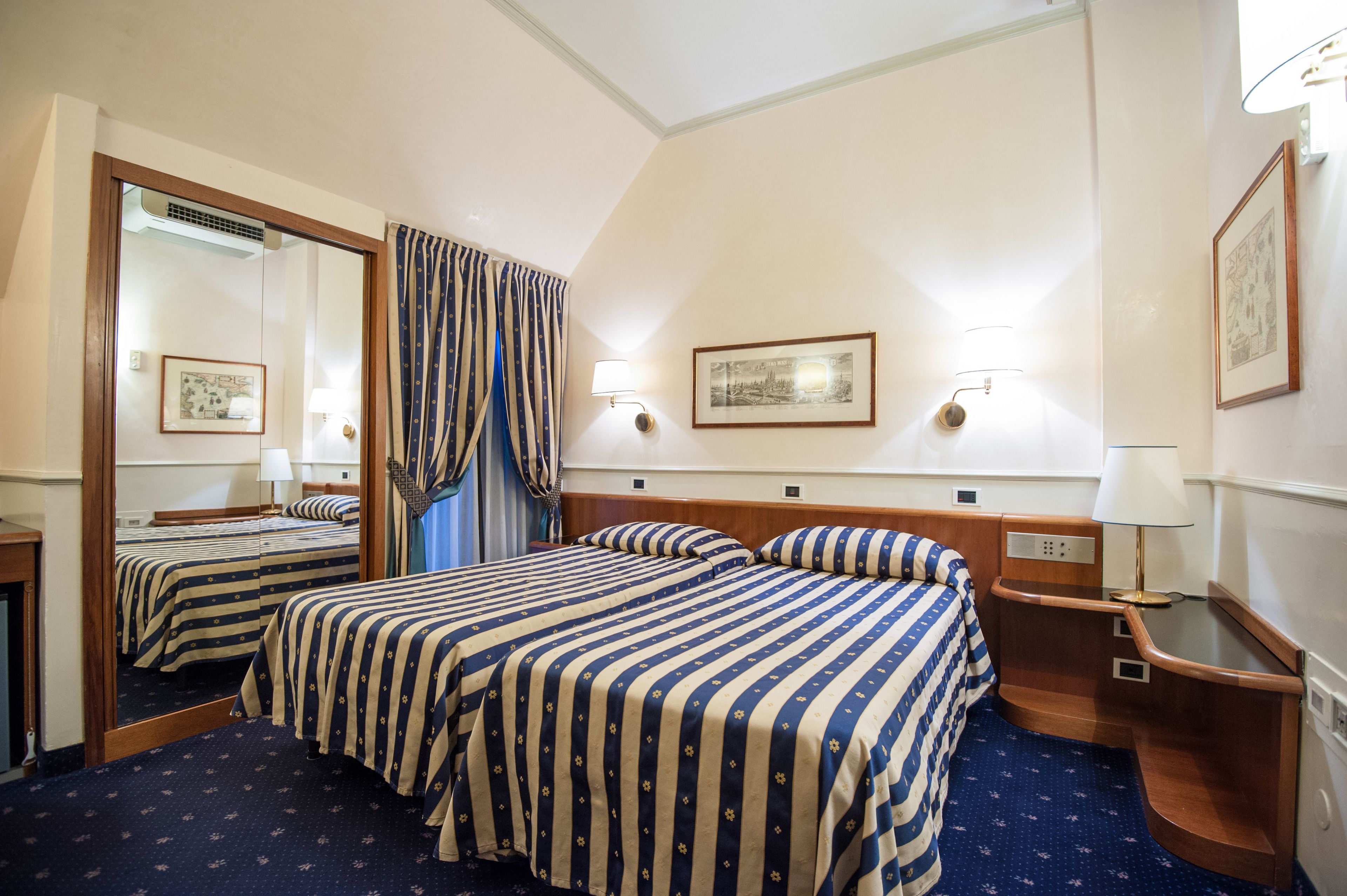 Une chambre d’hôtel avec deux lits, un grand miroir, une table de chevet avec une lampe et un tableau encadré au mur.