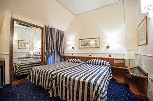 Een hotelkamer met twee bedden, een grote spiegel, een nachtkastje met een lamp en een lijst aan de muur.