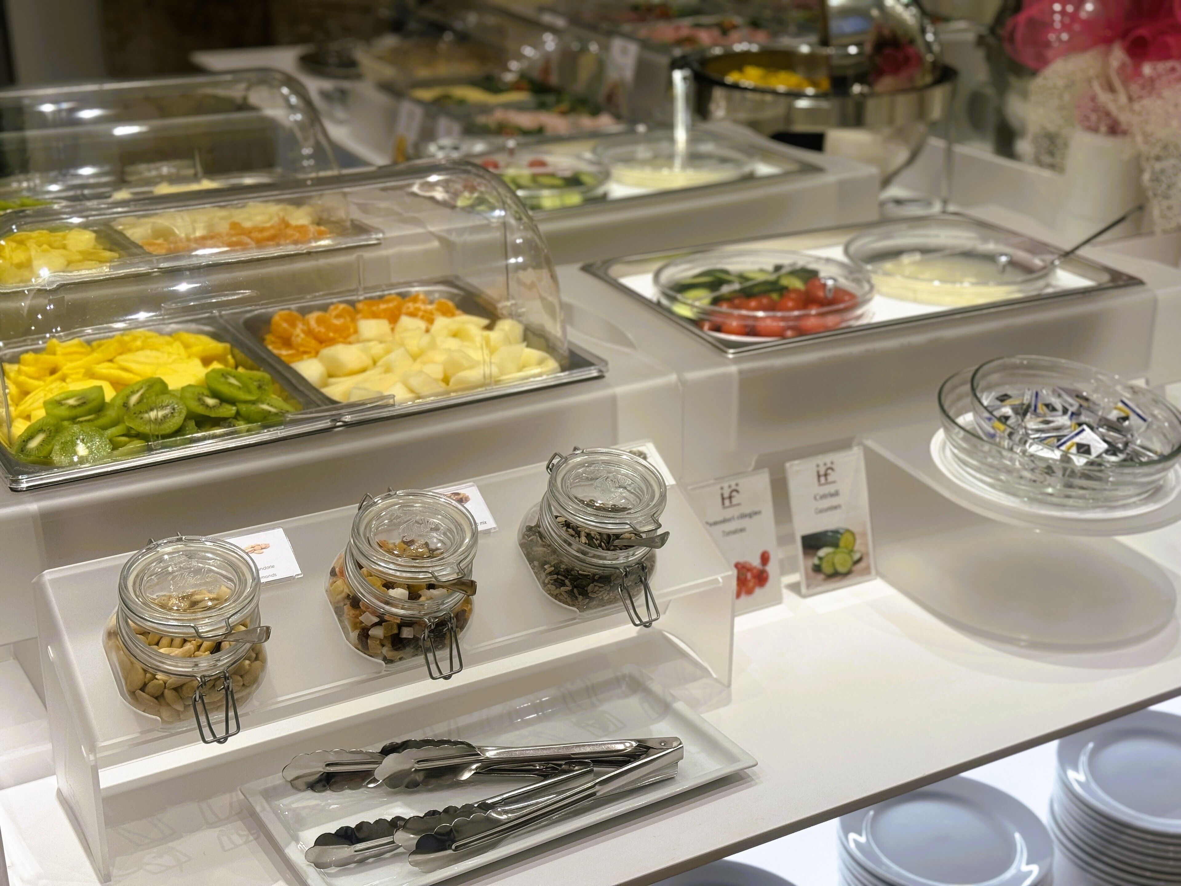 A buffet with various food items in clear containers, including fruits, nuts, and condiments.