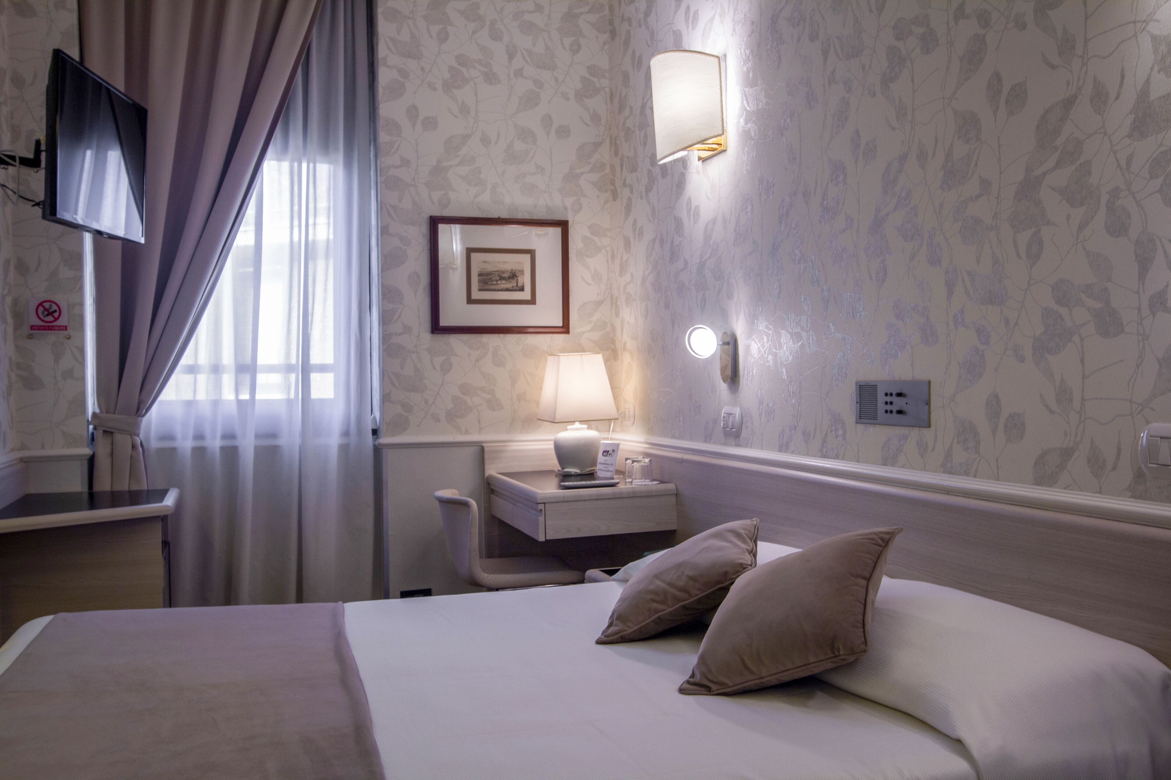 Una habitación de hotel con cama, mesita de noche, lámpara y televisor montado en la pared.