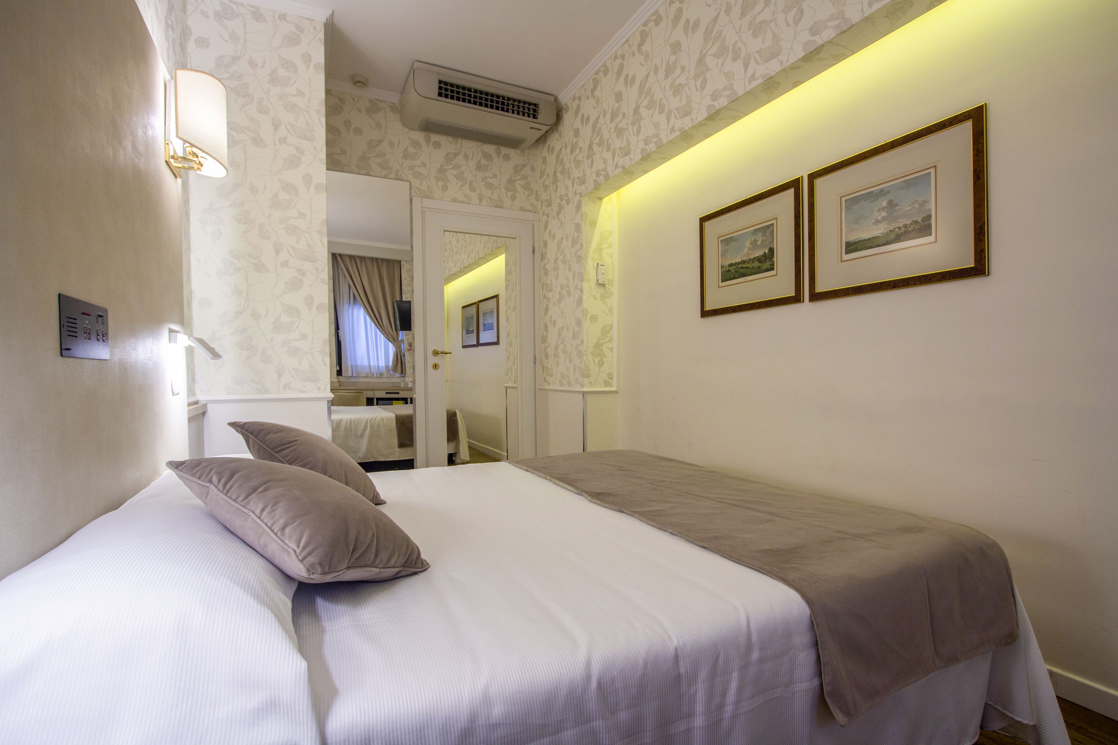 Habitación de hotel con cama, dos almohadas, lámpara de noche y dos cuadros en la pared.