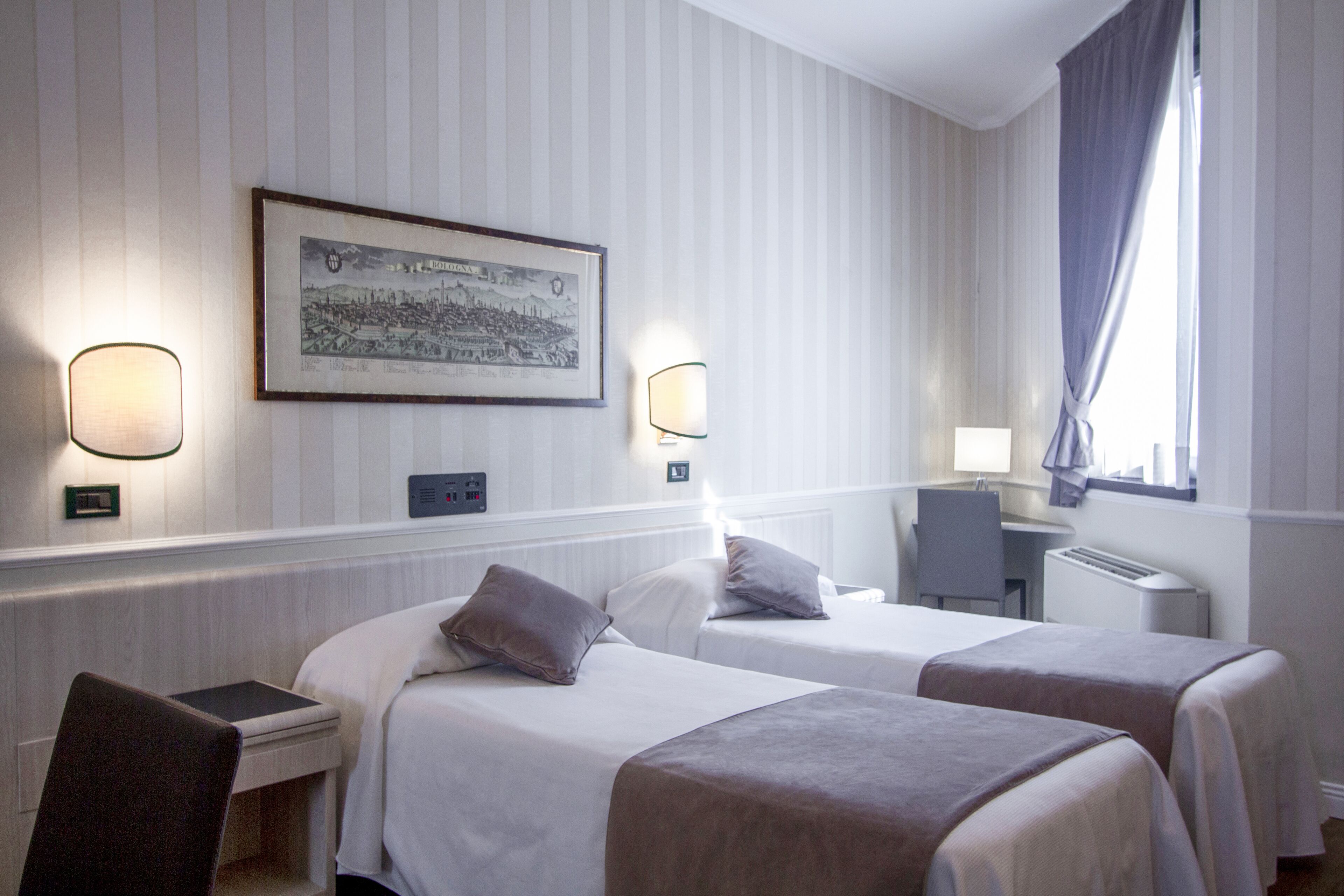 Habitación de hotel con dos camas, un escritorio, una silla, un cuadro en la pared y una ventana con cortinas.