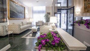 Un hall d’hôtel avec un sol en marbre, un grand tableau, un canapé, une table basse et des fleurs violettes.