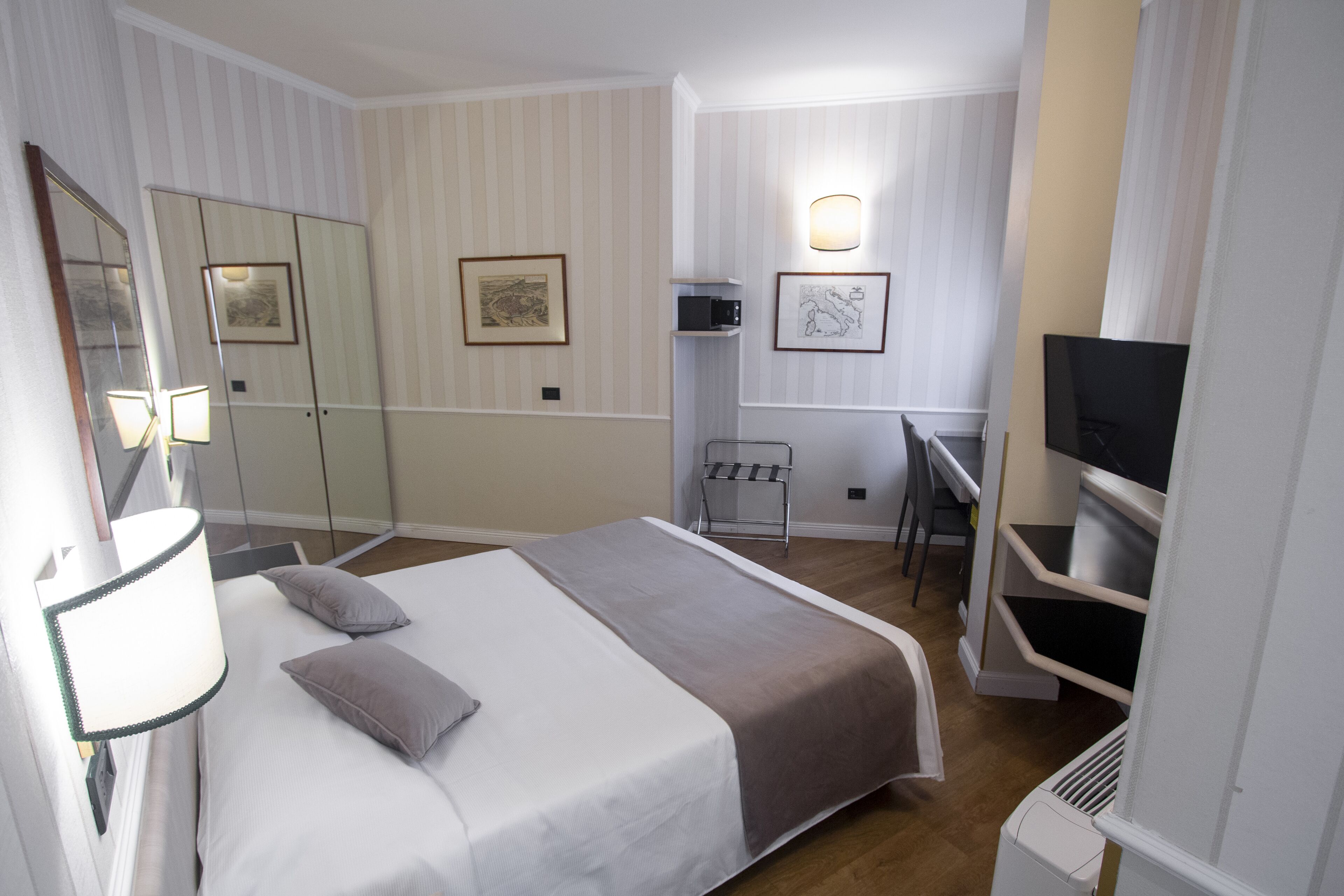 A hotel room with a bed, a desk, a TV, and a mirror.