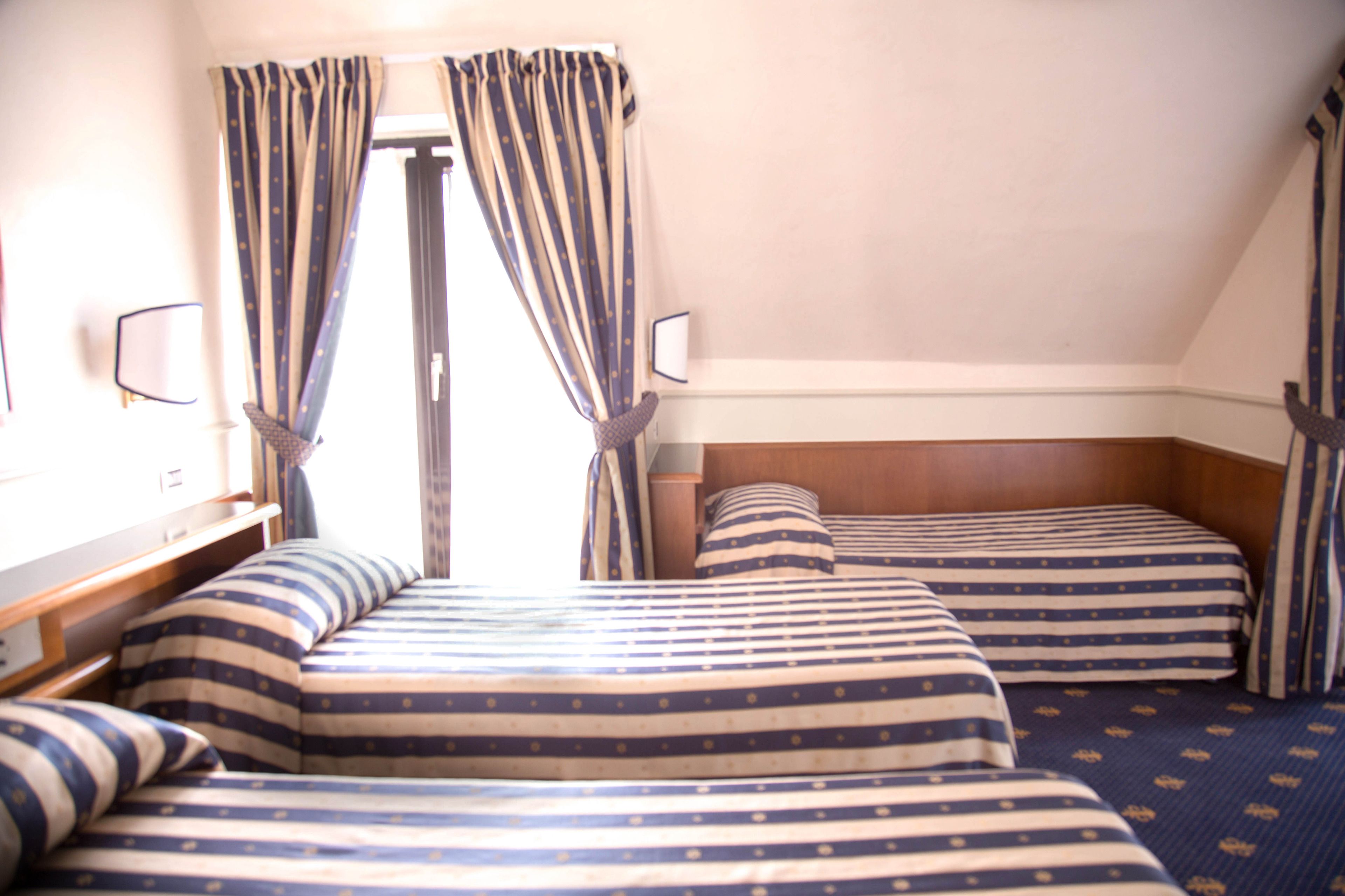 Habitación de hotel con dos camas, ropa de cama a rayas, cabecera de madera y una ventana con cortinas.