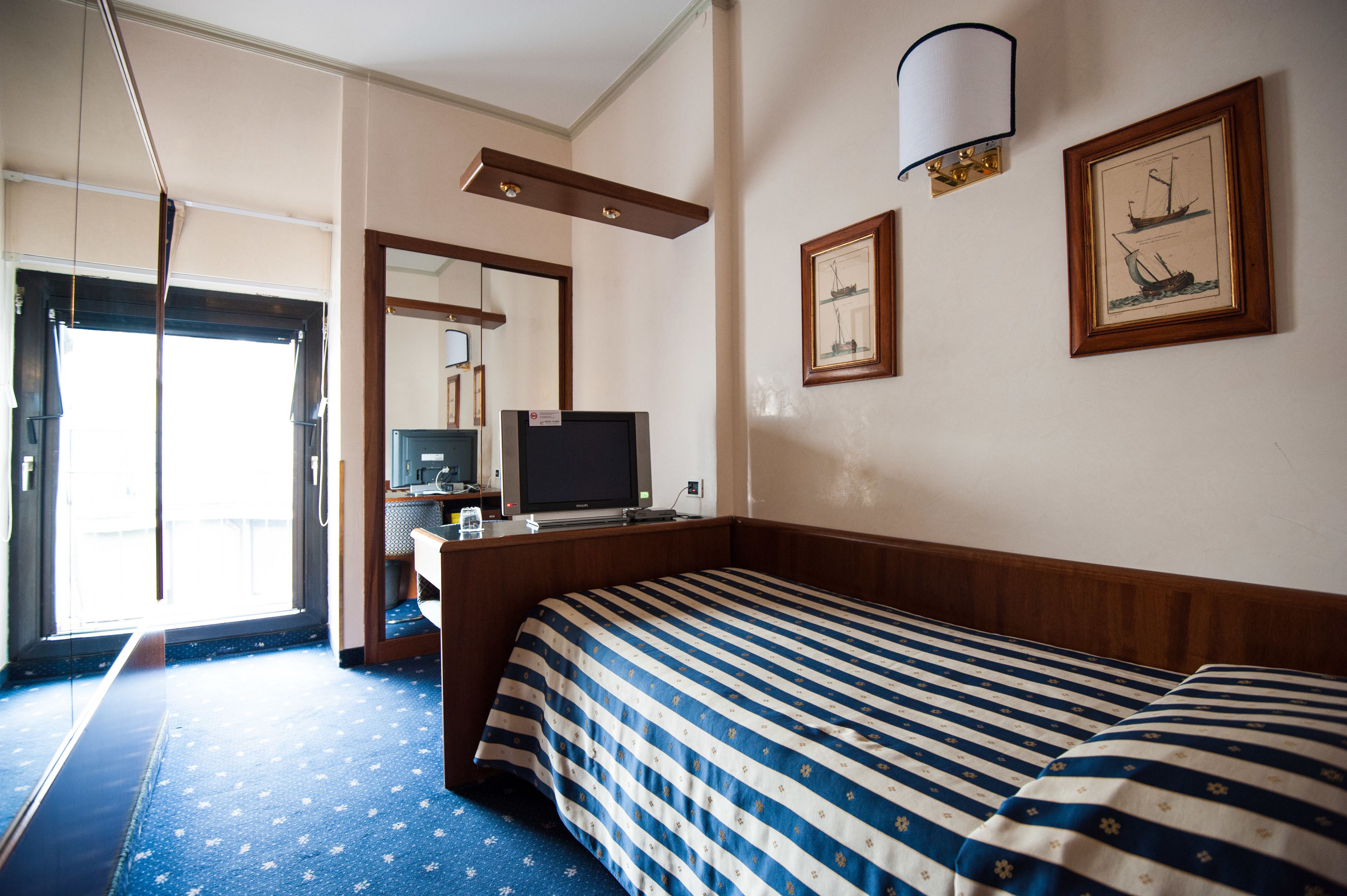 A hotel room with a bed, a television, a desk with a computer, and a window with curtains.