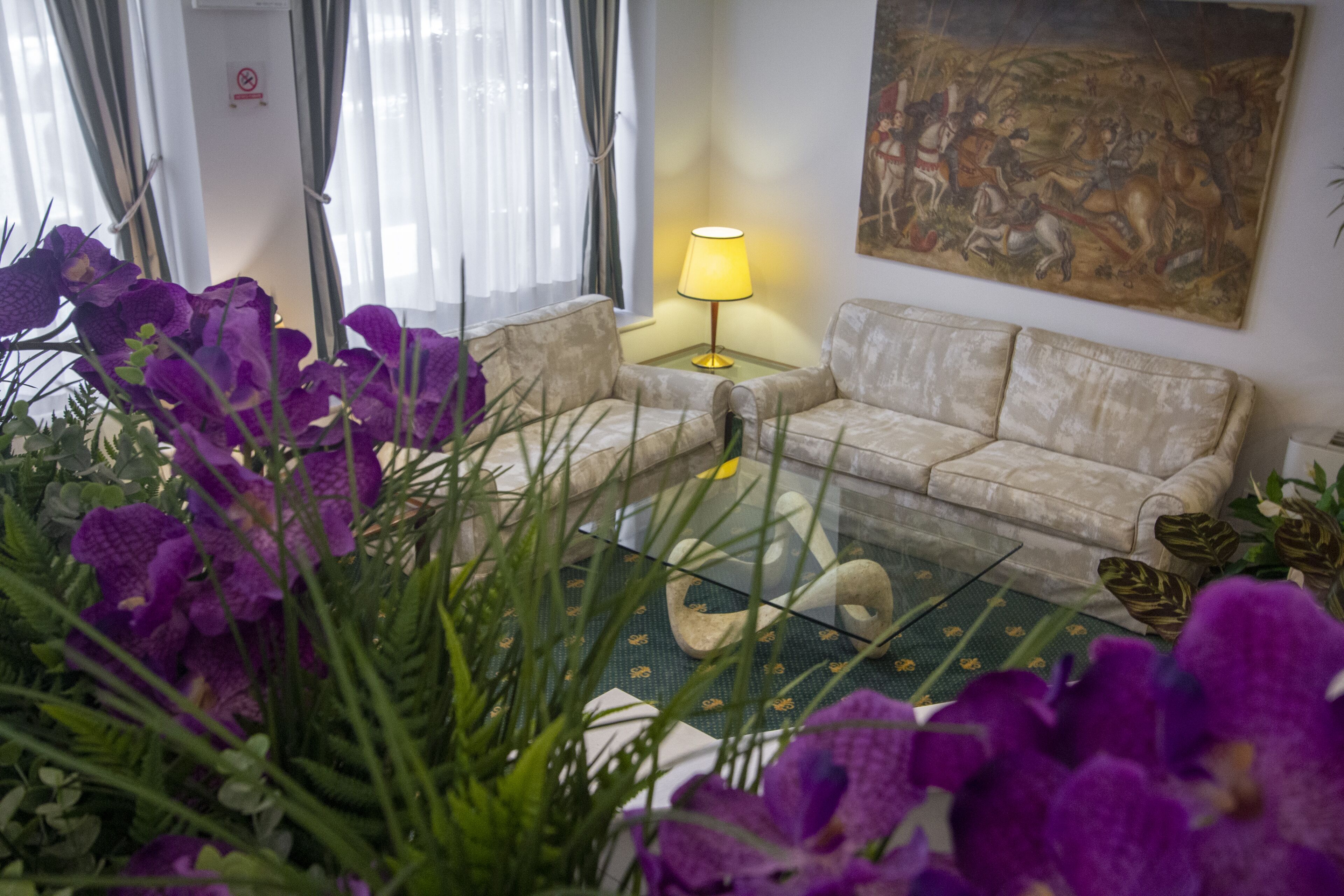 Un salon avec un canapé, une table basse en verre et des fleurs violettes.