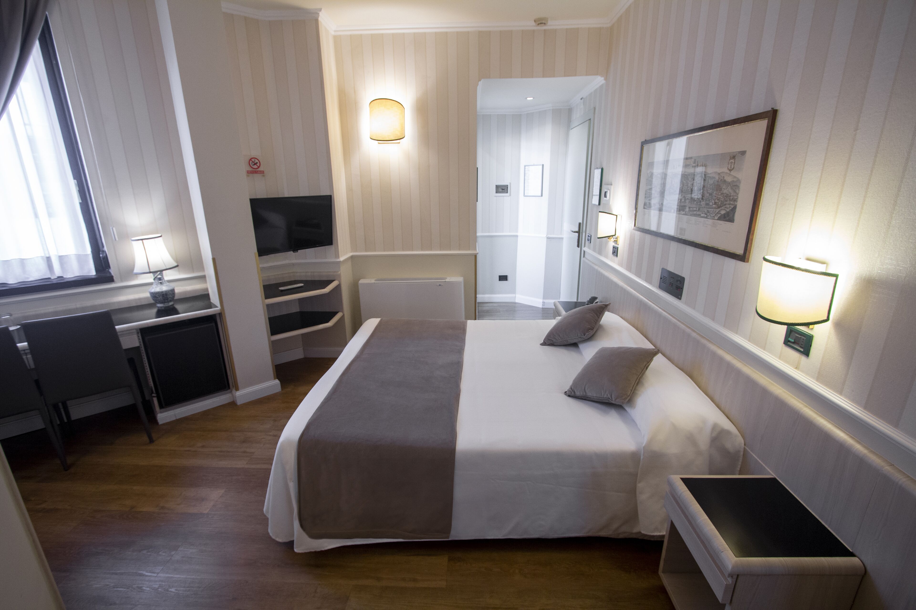 Une chambre d’hôtel comprenant un lit, une table de chevet, une télévision et un bureau avec une chaise.