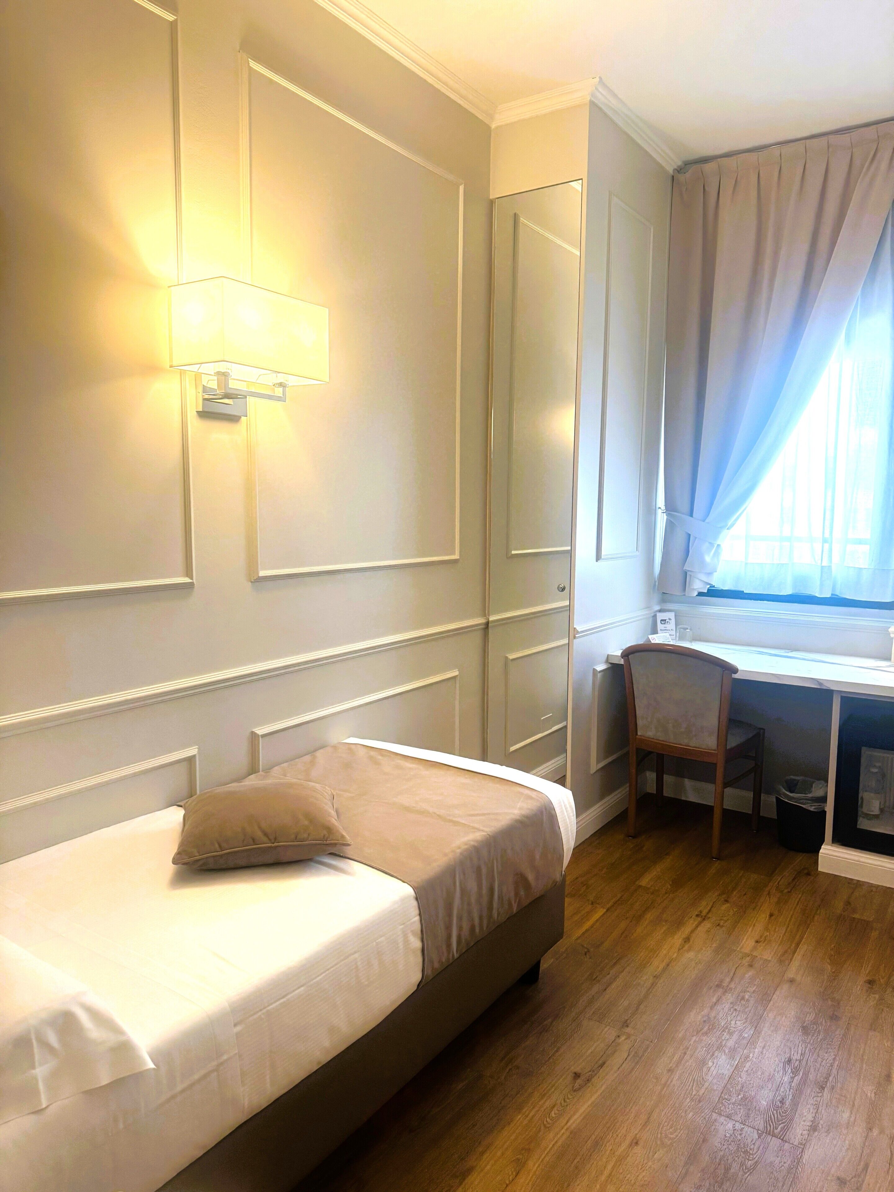 A hotel room with a bed, a desk, a chair, and a window with curtains.