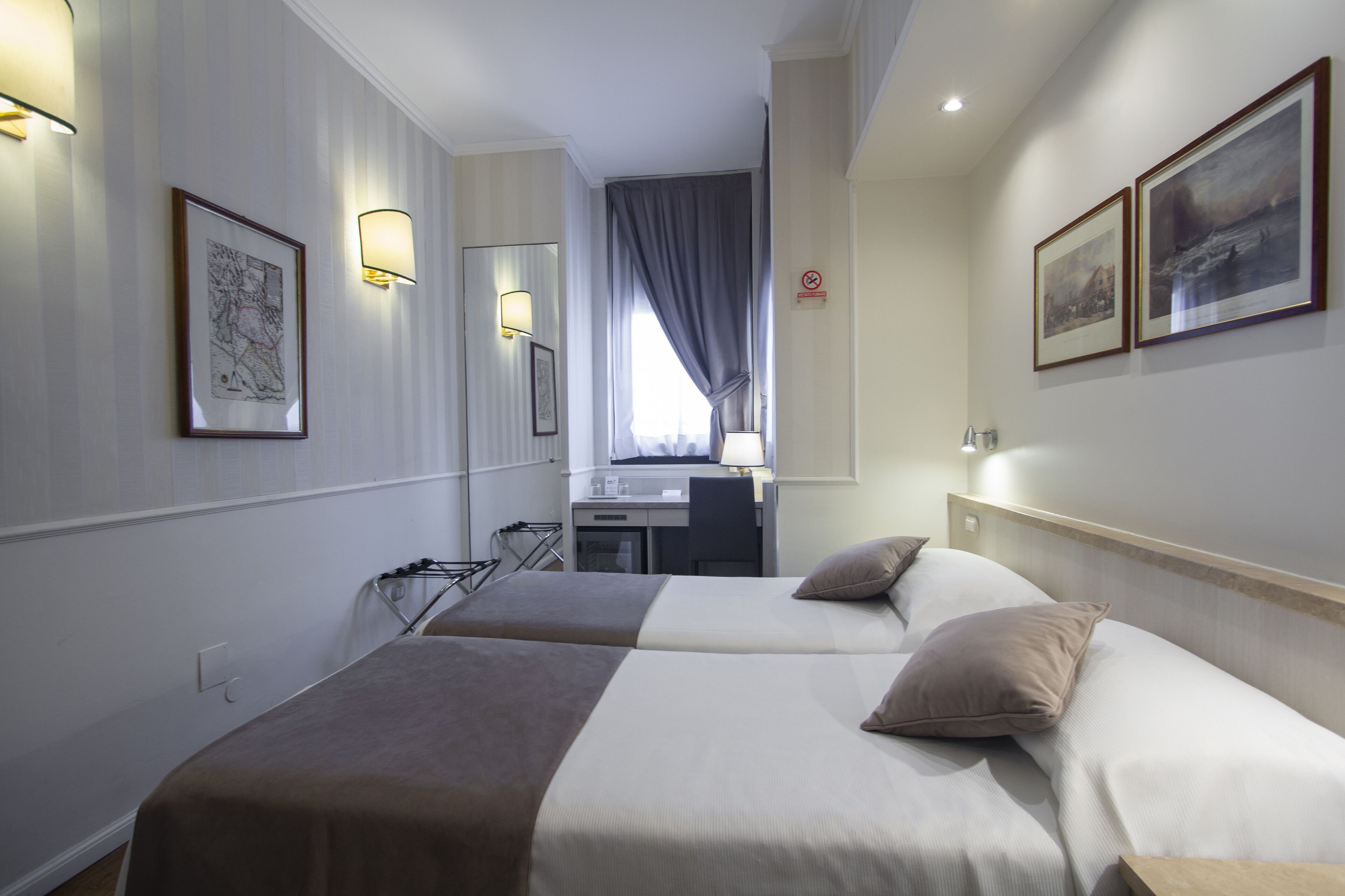 Habitación de hotel con dos camas, un escritorio y una silla. Hay luces fijadas a la pared y cuadros enmarcados.
