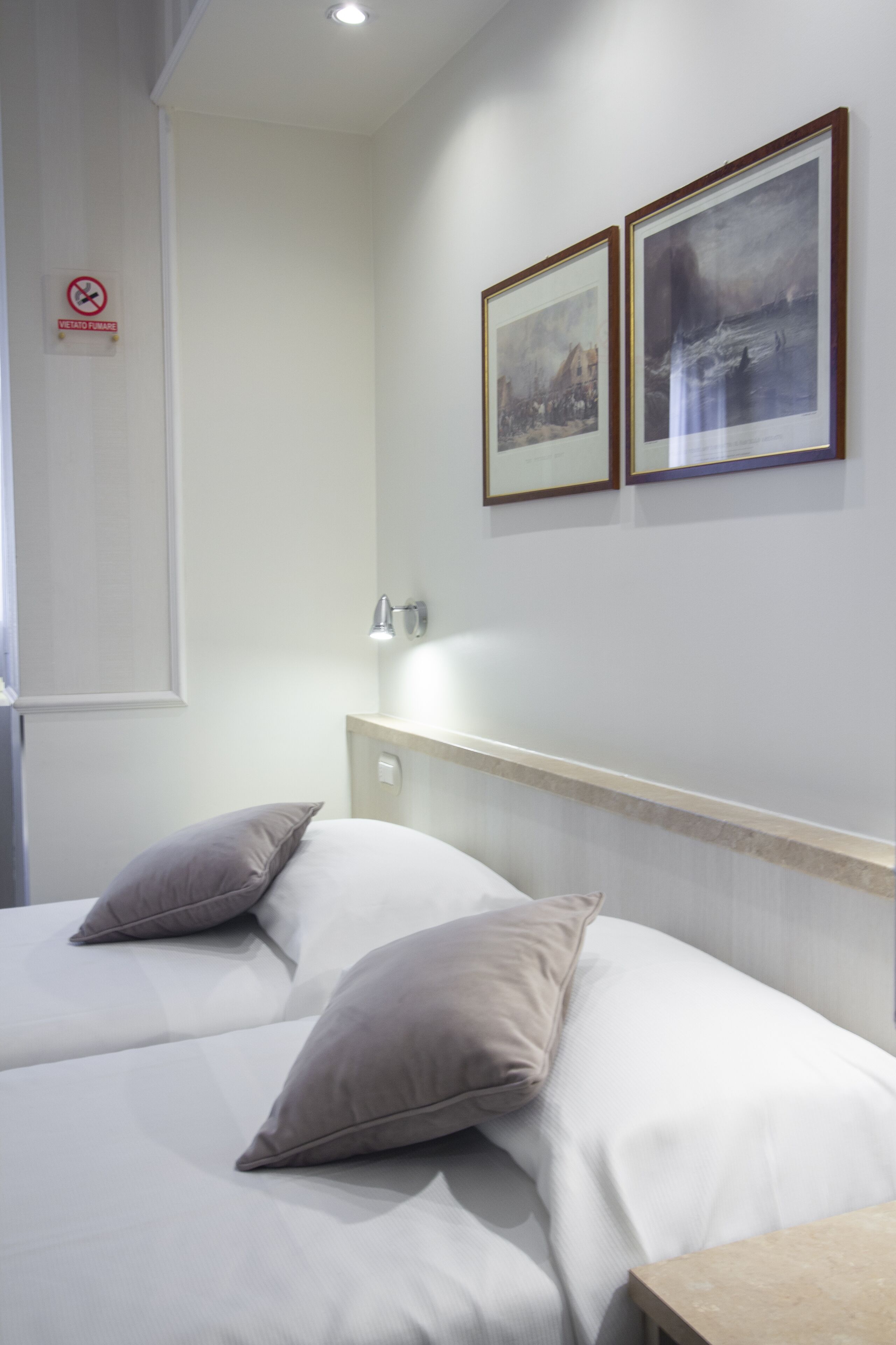 Een hotelkamer met twee bedden, een nachtkastje, een wandlamp en twee ingekaderde foto's.