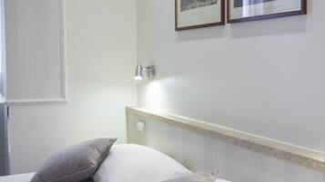 Una habitación de hotel con dos camas, una mesita de noche, una lámpara de pared y dos cuadros enmarcados.