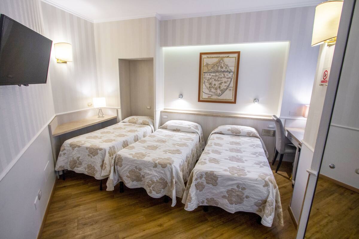 A hotel room with two single beds, a desk, a chair, a TV, and a framed map on the wall.