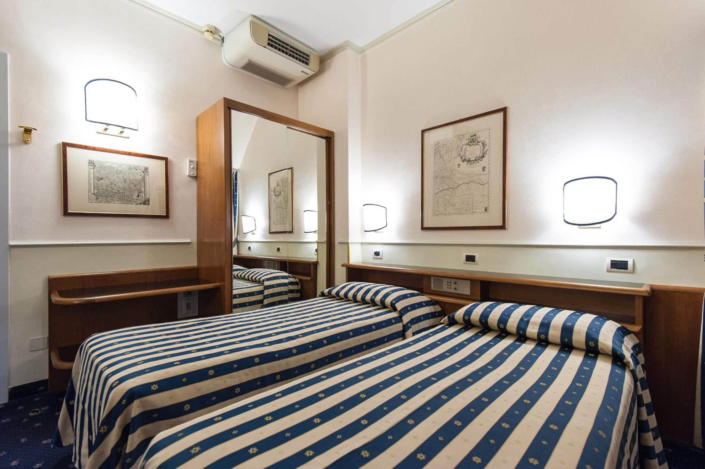Une chambre d’hôtel avec deux lits, un grand miroir et des œuvres d’art encadrées accrochées aux murs.