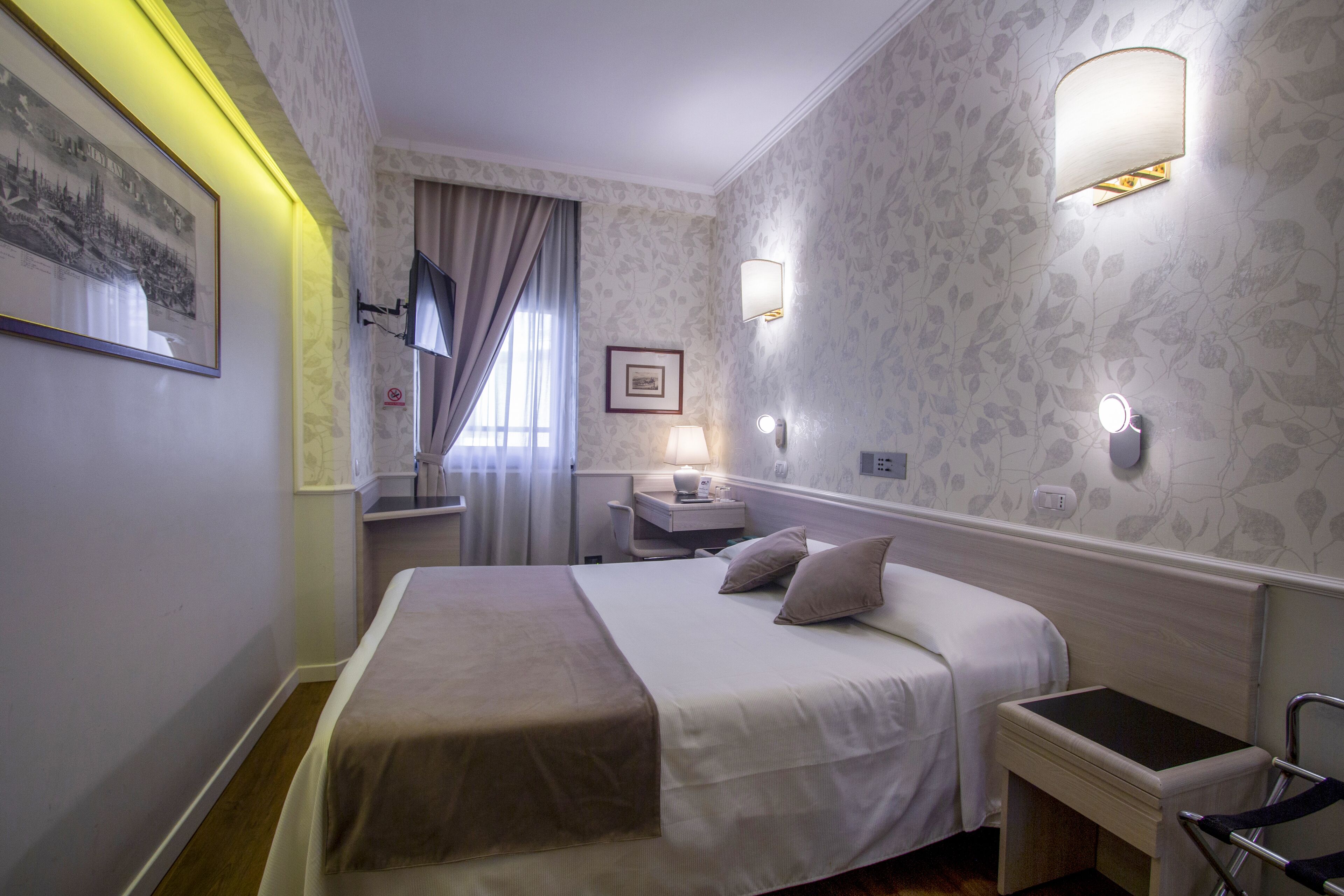 A hotel room with a bed, bedside tables, a desk, a chair, and a lamp.
