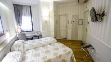 Camera d'albergo con due letti, una scrivania, una sedia, una TV a parete e una finestra con tende.