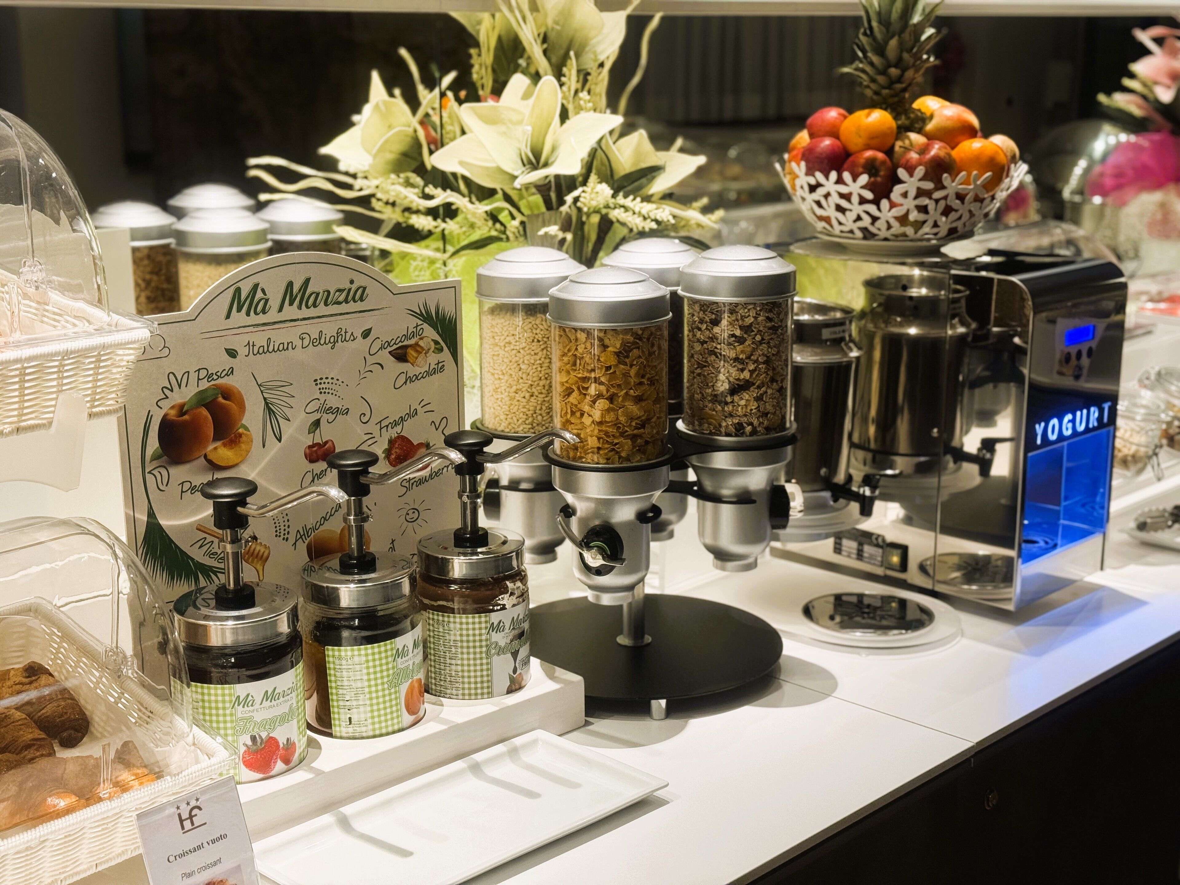 Een koffiehoek met diverse koffiezetapparaten, potten met toevoegingen en een bord waarop verschillende koffiesmaken staan aangegeven.