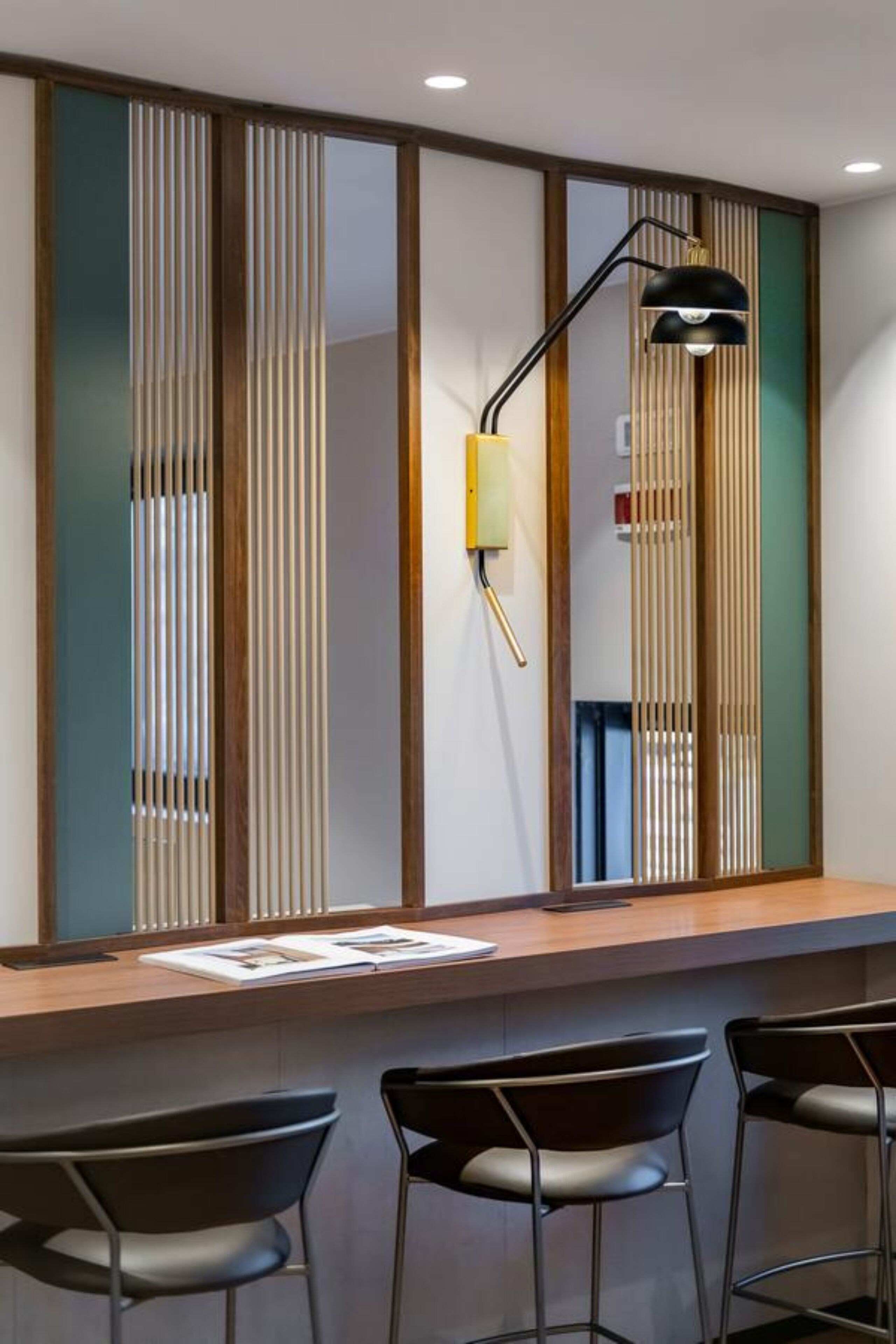 A modern bar area with a wooden counter, black bar stools, and a black pendant lamp.