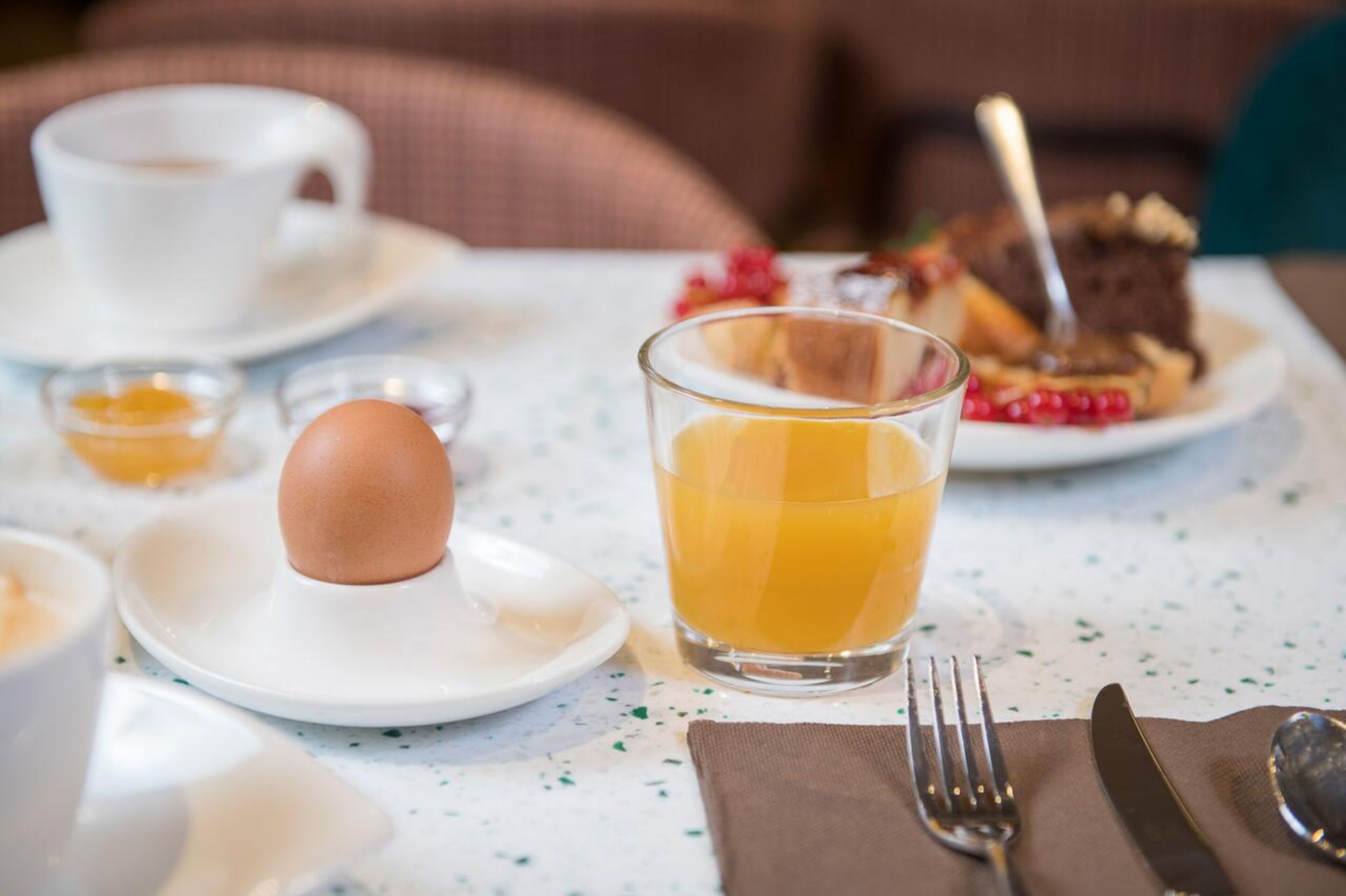 Une table mise pour le petit-déjeuner avec une tasse, un verre de jus d’orange, une assiette contenant une pâtisserie et un œuf dur.