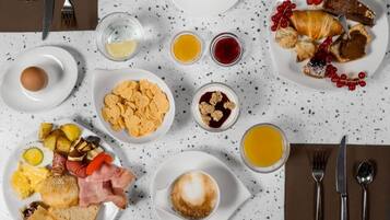 Une table dressée pour le petit-déjeuner, avec différents plats, notamment des œufs, des toasts, des croissants et des fruits.