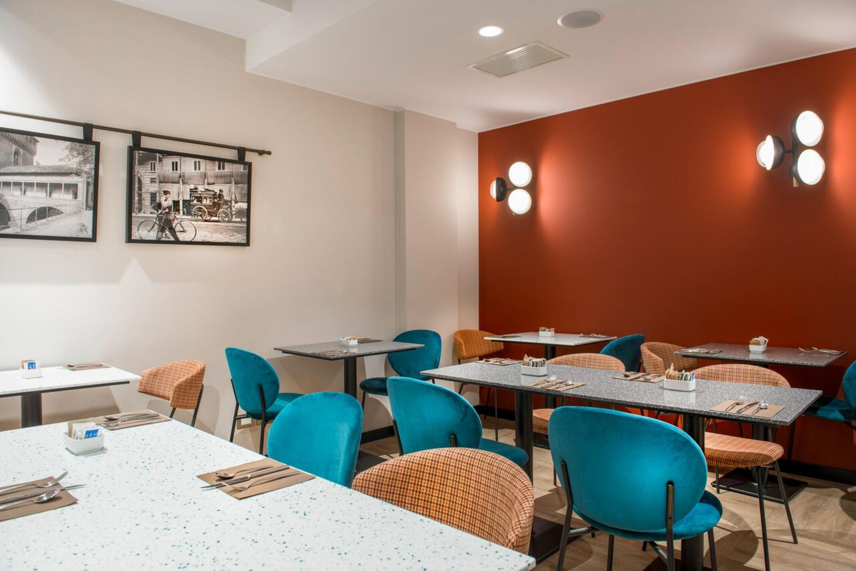A hotel dining area with tables and chairs, framed pictures on the wall, and a red accent wall.