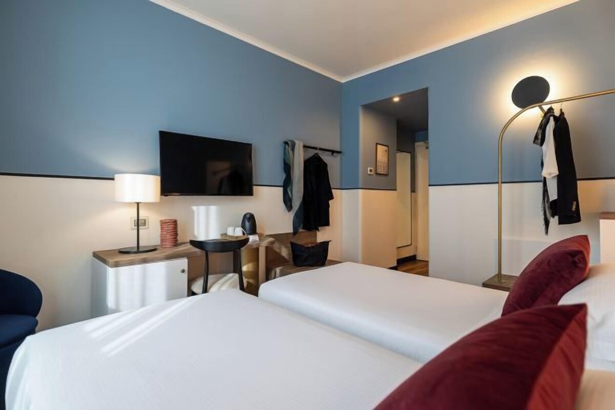 Une chambre d’hôtel avec deux lits, un bureau avec une chaise, une télévision et un miroir.