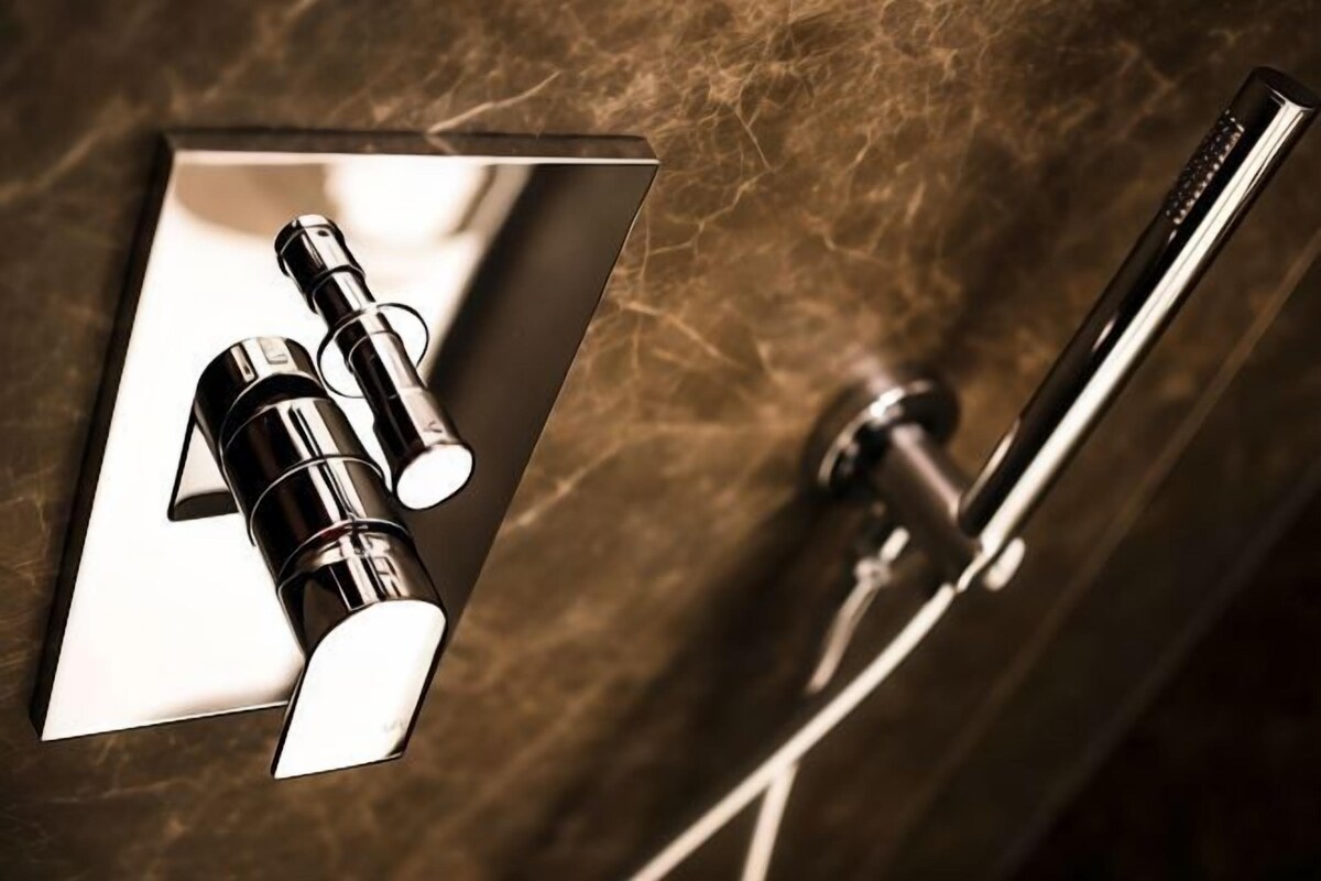 Une salle de bain au design moderne, dotée d’un miroir, d’une douchette et d’un robinet mural.