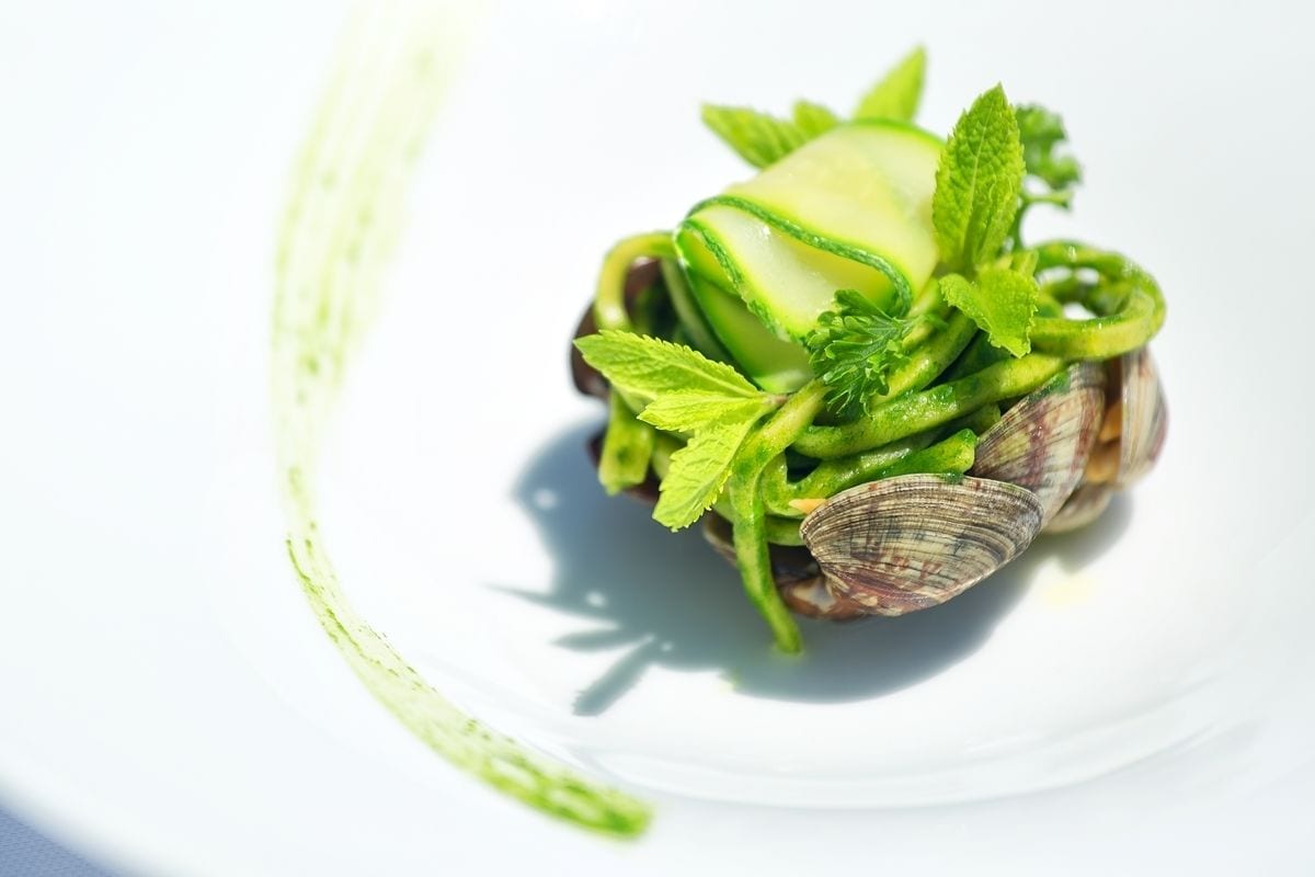 A dish with clams, green vegetables, and mint leaves on a white plate.