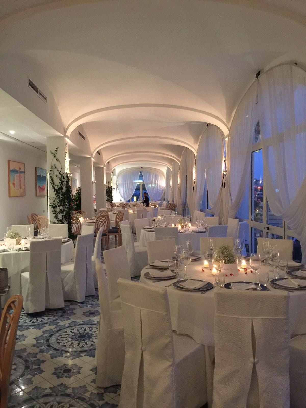 Une salle à manger élégante, avec des tables et des chaises blanches, un éclairage raffiné et une vue sur la ville au crépuscule.