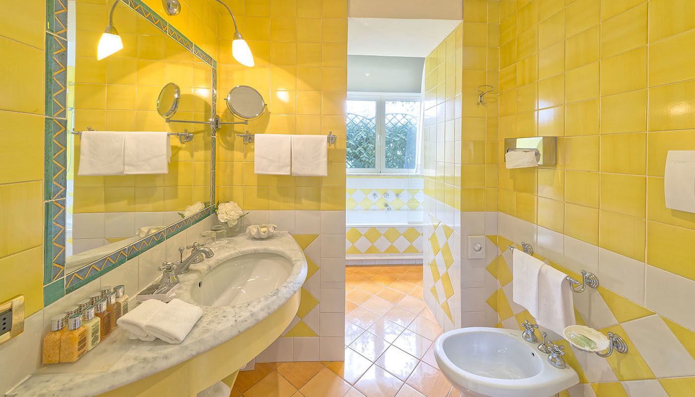 A bathroom with yellow tiles, a sink, a mirror, and a window with a view.