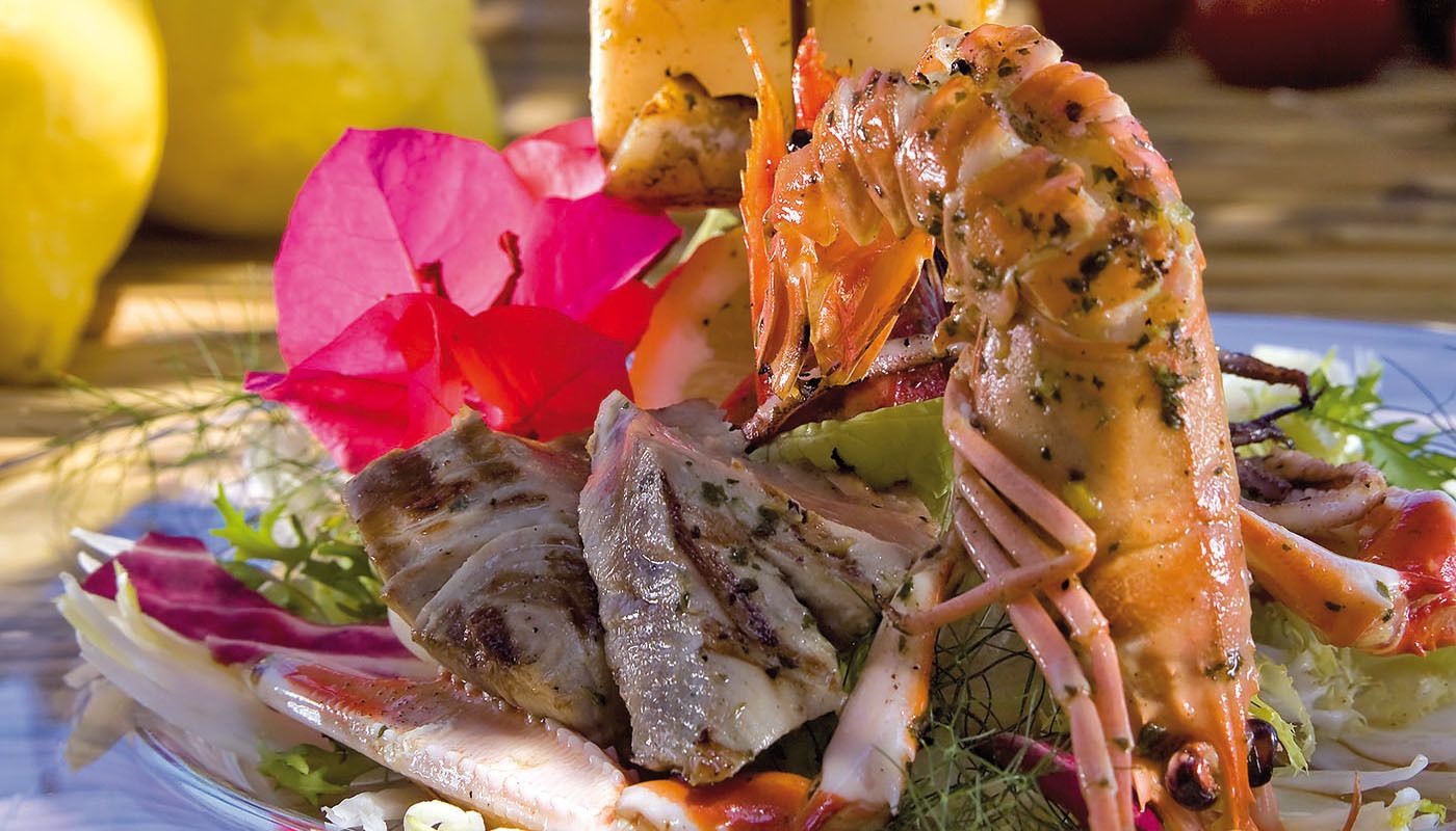 A seafood dish with grilled fish and shrimp, garnished with herbs and flowers.