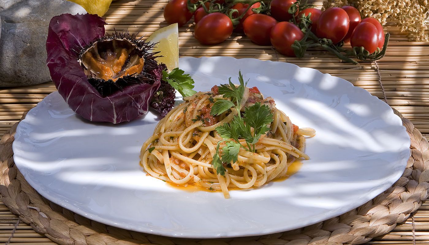 A plate of spaghetti with a garnish of parsley, a lemon wedge, and a decorative shell on a white plate.