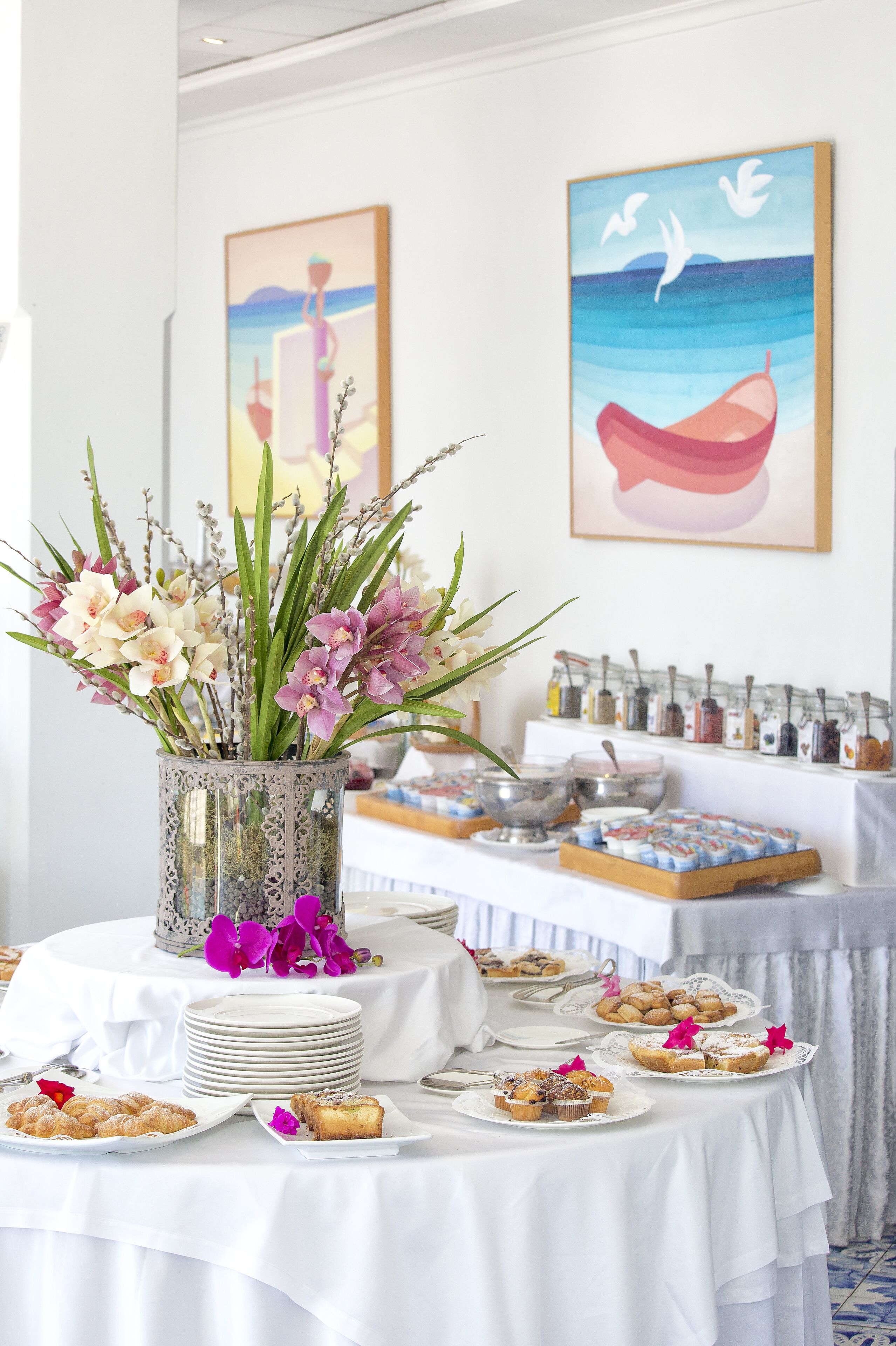 A buffet table with white tablecloths, a floral centerpiece, and various food items.