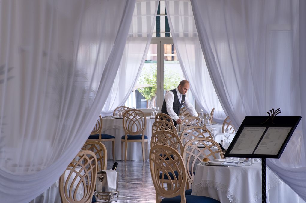 A restaurant with white drapes, wooden chairs, and a menu stand.