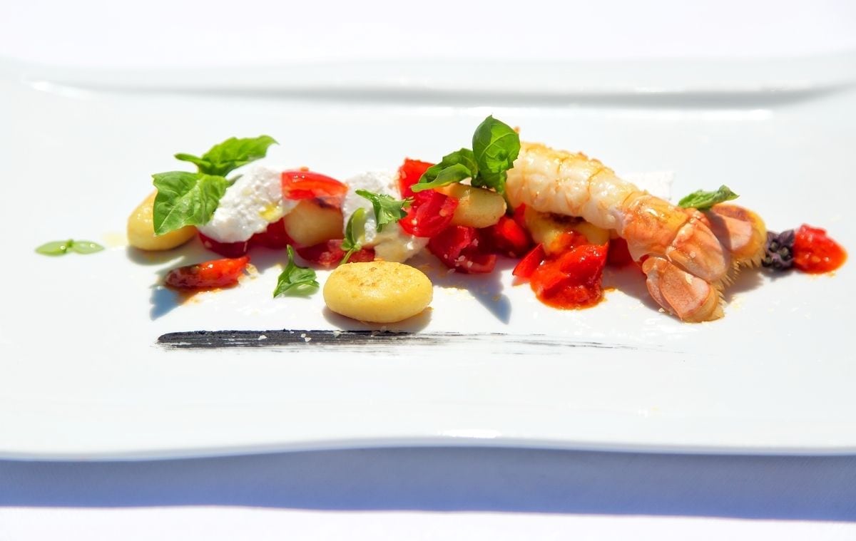 A white plate with a seafood dish, including shrimp, cherry tomatoes, and a dollop of cream.