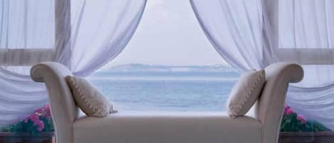 A white sofa with a view of the sea through sheer curtains.