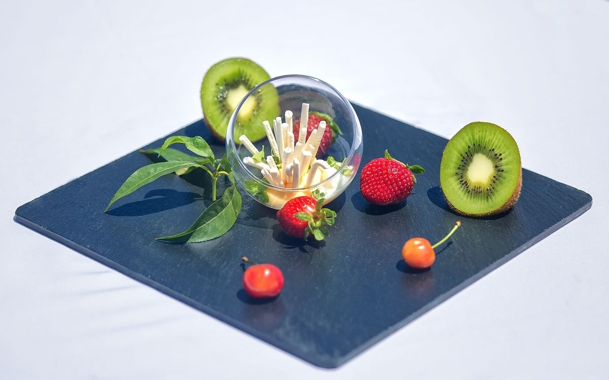 A black slate serving tray with sliced kiwi, strawberries, and cherries, and a glass bowl with toothpicks.