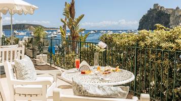 Une terrasse avec une table dressée pour le petit-déjeuner, d’où l’on aperçoit une marina avec des bateaux et, au loin, un bâtiment historique.
