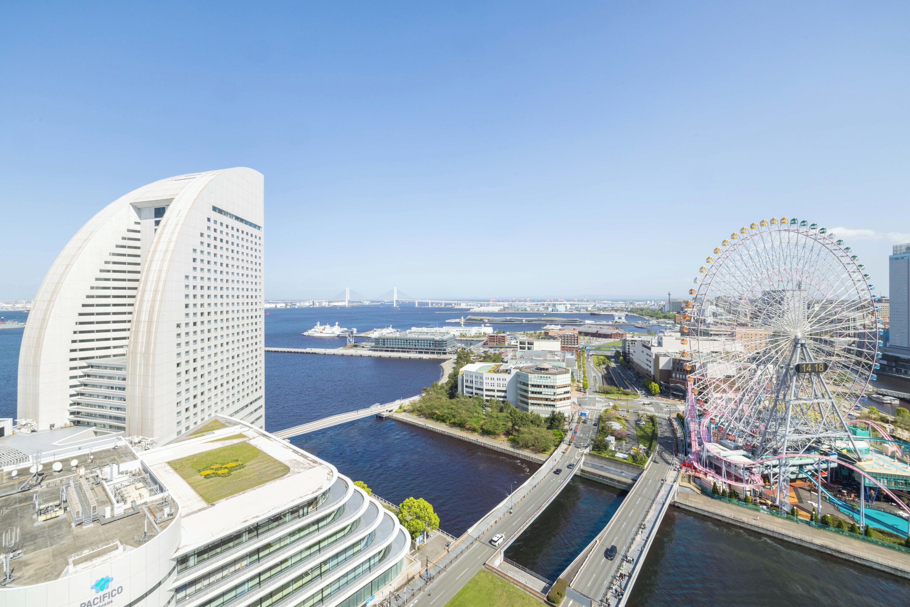 A modern hotel with a curved facade, a waterfront view, and a Ferris wheel in the background.