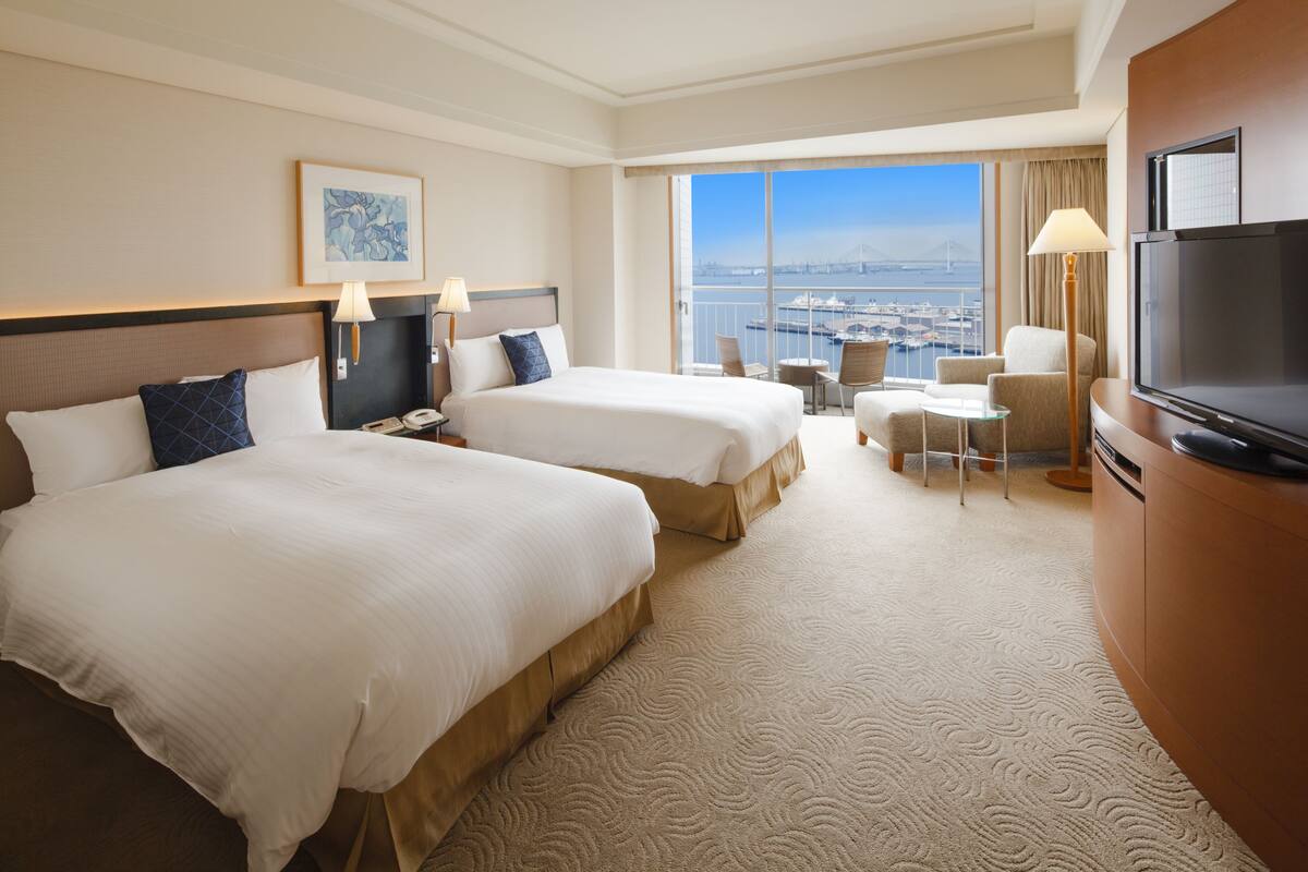 Habitación de hotel con dos camas, televisión, escritorio y vista a la ciudad.