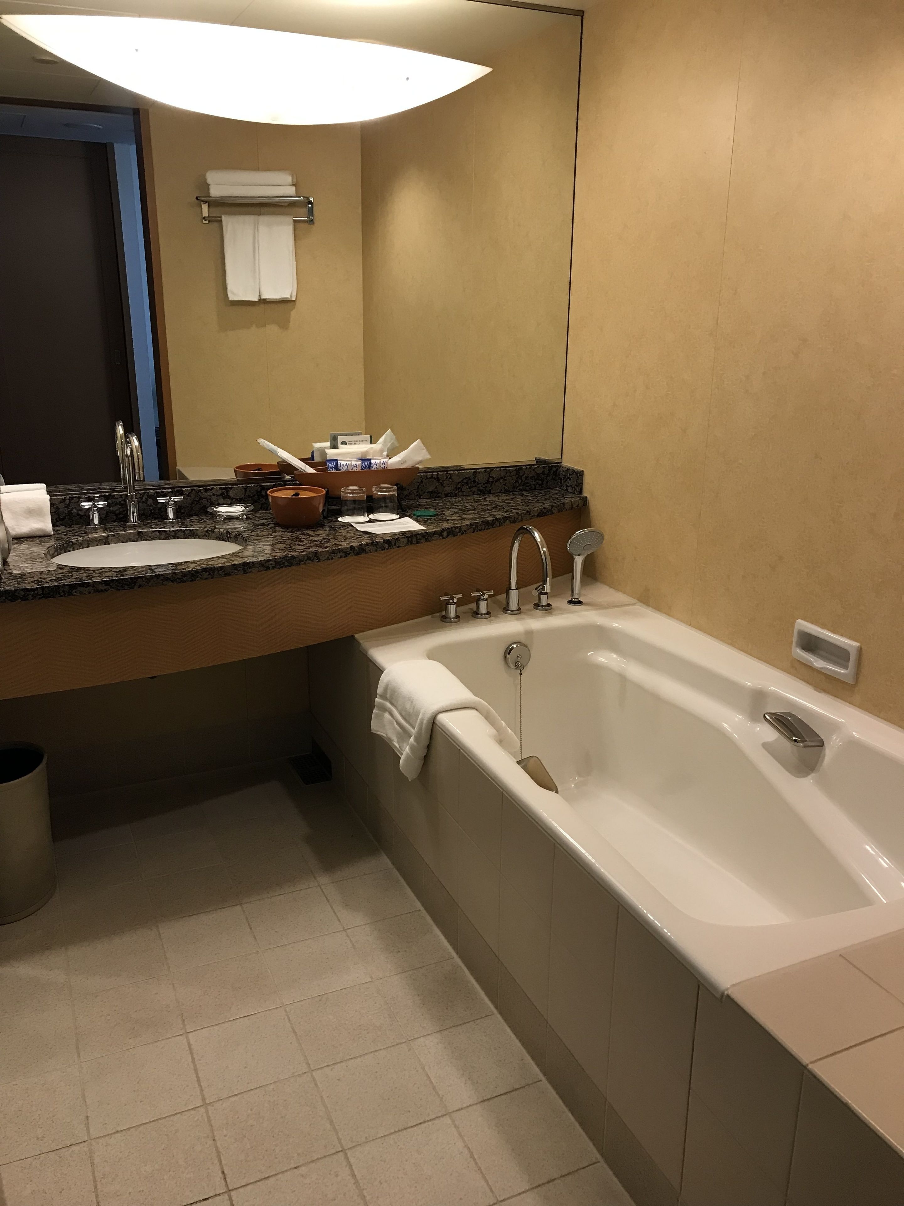 Une salle de bain moderne avec une grande baignoire, un lavabo doté d’un plan de travail en granit et un miroir au-dessus du lavabo.