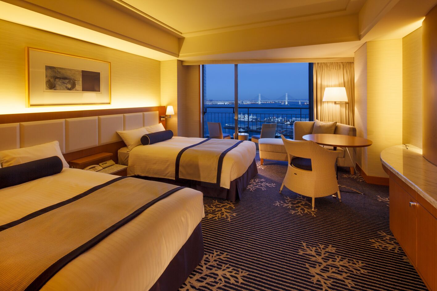 Ein Hotelzimmer mit zwei Betten, einem kleinen Tisch, einem Stuhl und Blick auf eine Brücke und Stadtansicht.