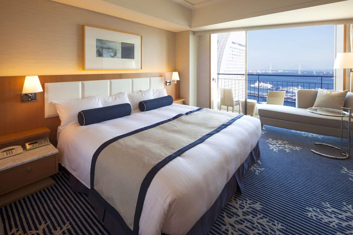 Habitación de hotel con una cama grande, un escritorio con teléfono, una silla y vistas a la ciudad y al puente.