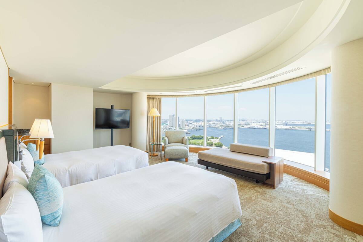 Habitación de hotel con dos camas, televisión, ventana grande con vista a la ciudad y techo curvo.