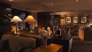 A modern hotel lobby with sofas, a coffee table, a vase with flowers, and a bar area.