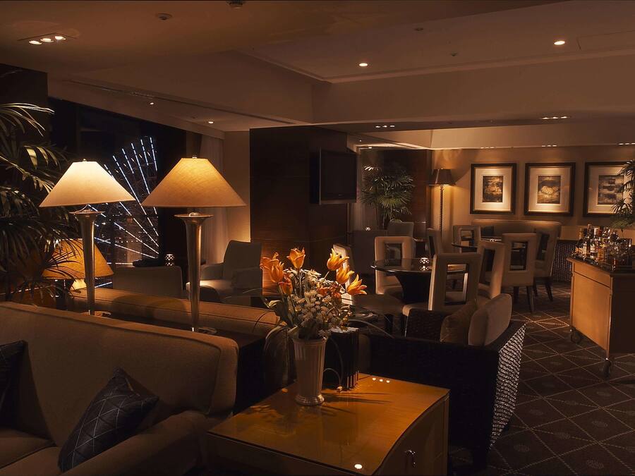 A modern hotel lobby with sofas, a coffee table, a vase with flowers, and a bar area.