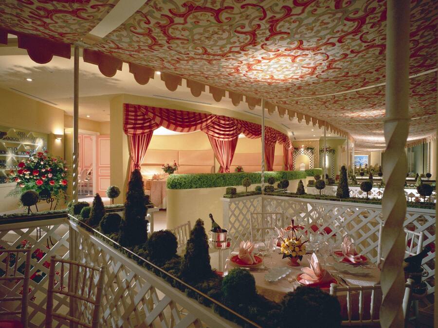 A well-lit indoor space with a decorative ceiling, a dining area with a table set for a meal, and a staircase with a railing.