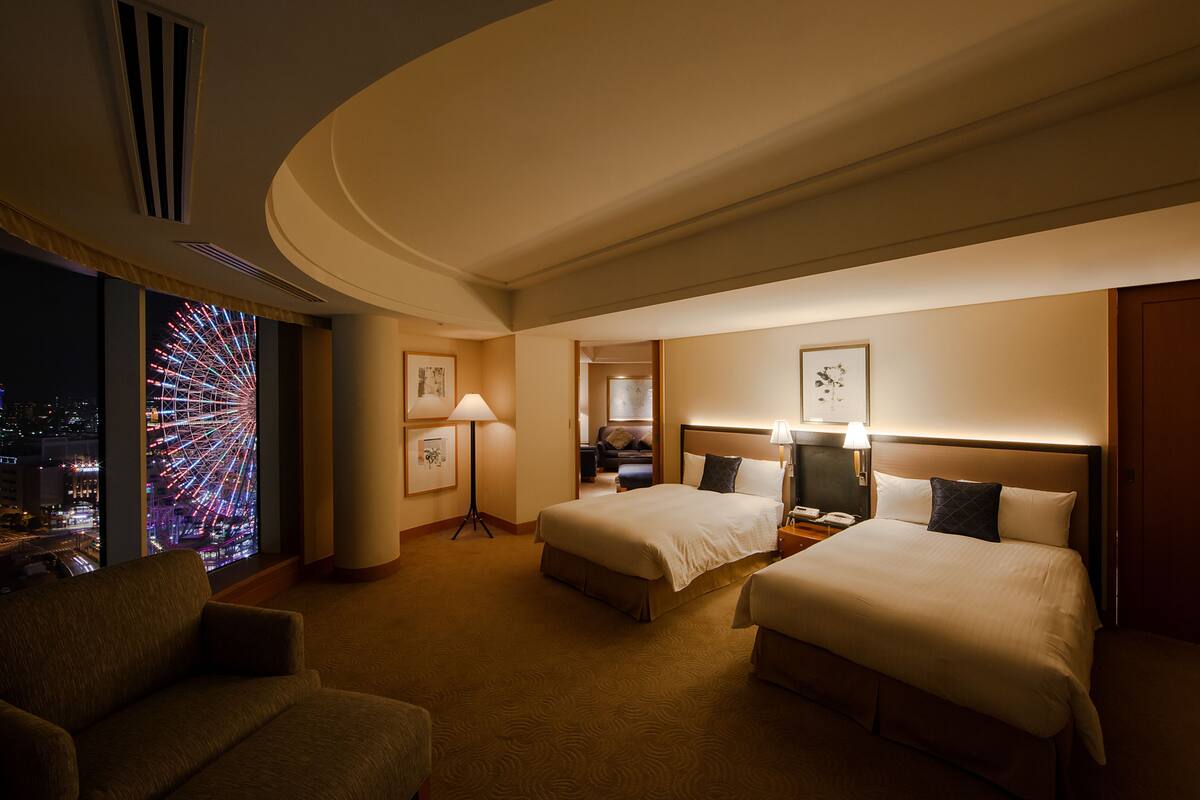 Habitación de hotel con dos camas, un sofá, un ventanal grande con vistas a la ciudad y un adorno en la pared.