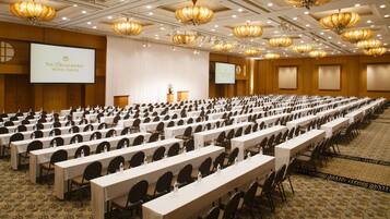 Un salón de conferencias en The Yokohama Bay Hotel Tokyo con filas de mesas y sillas, un atril y una pantalla grande.