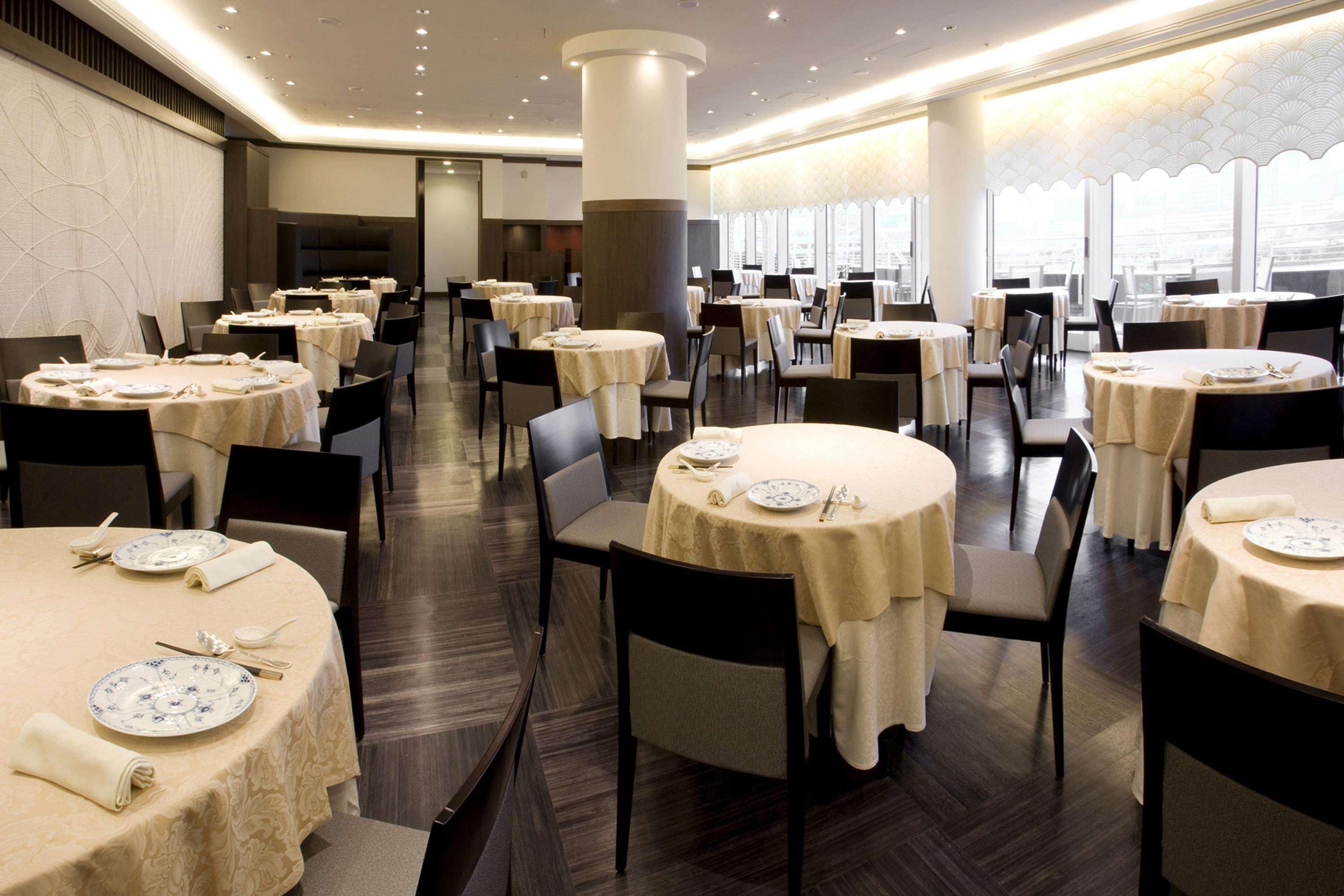 A spacious dining area with round tables, chairs, and a city view through large windows.